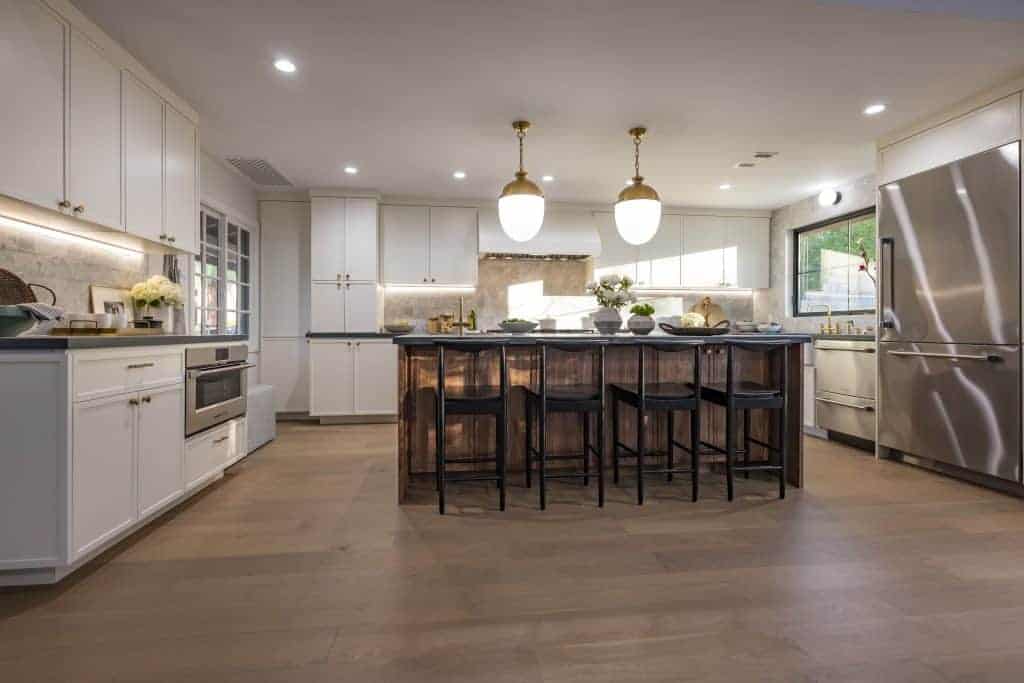 Spacious kitchen with white cabinets, wooden island with black stools, and brass pendant lights