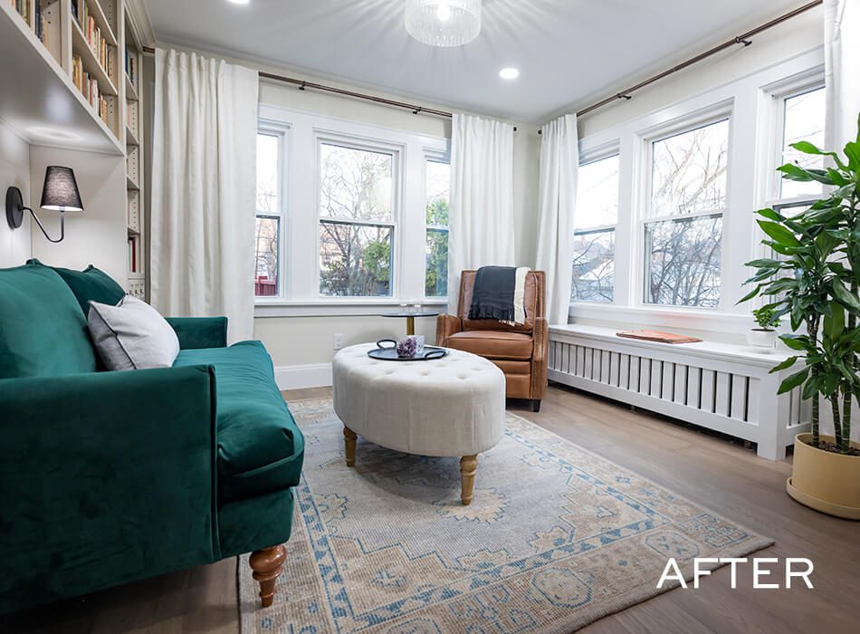 Bright sitting room with green sofa, round ottoman, and large windows with white curtains