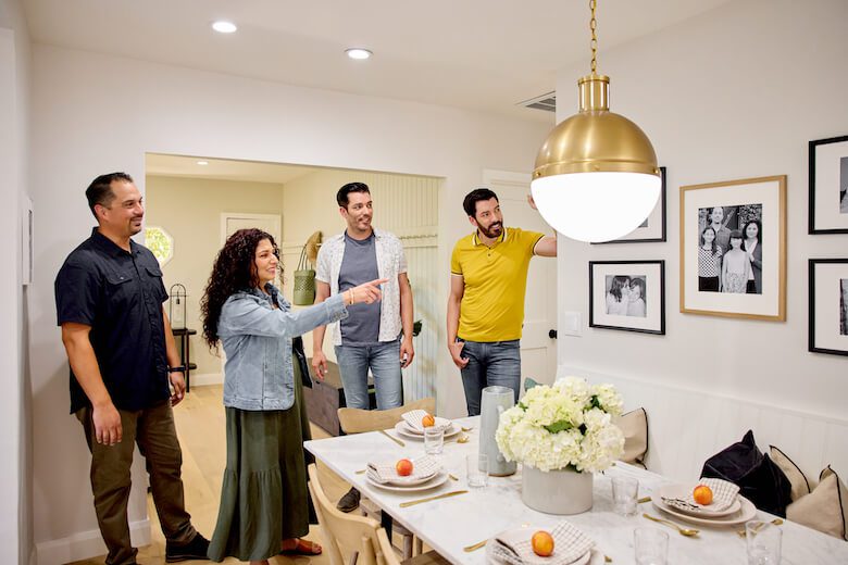 Group of four people admiring dining room with large gold light fixture and framed photos on the wall
