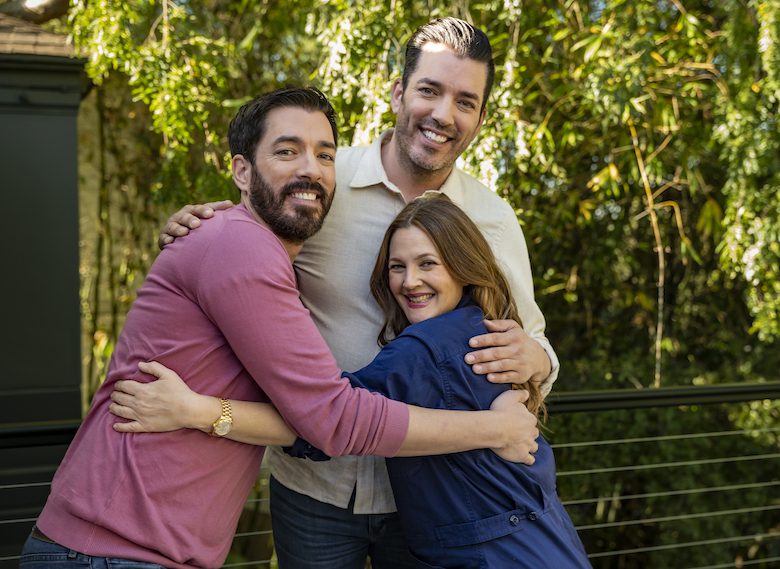 Drew and Jonathan hugging and smiling with Drew Barrymore outdoors with greenery in the background