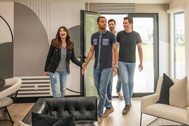 Four people entering a modern living room with abstract wall art, contemporary furniture, and large glass doors