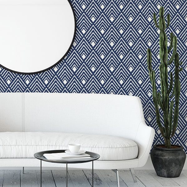 White curved sofa with round mirror, geometric blue wallpaper, and a tall potted cactus