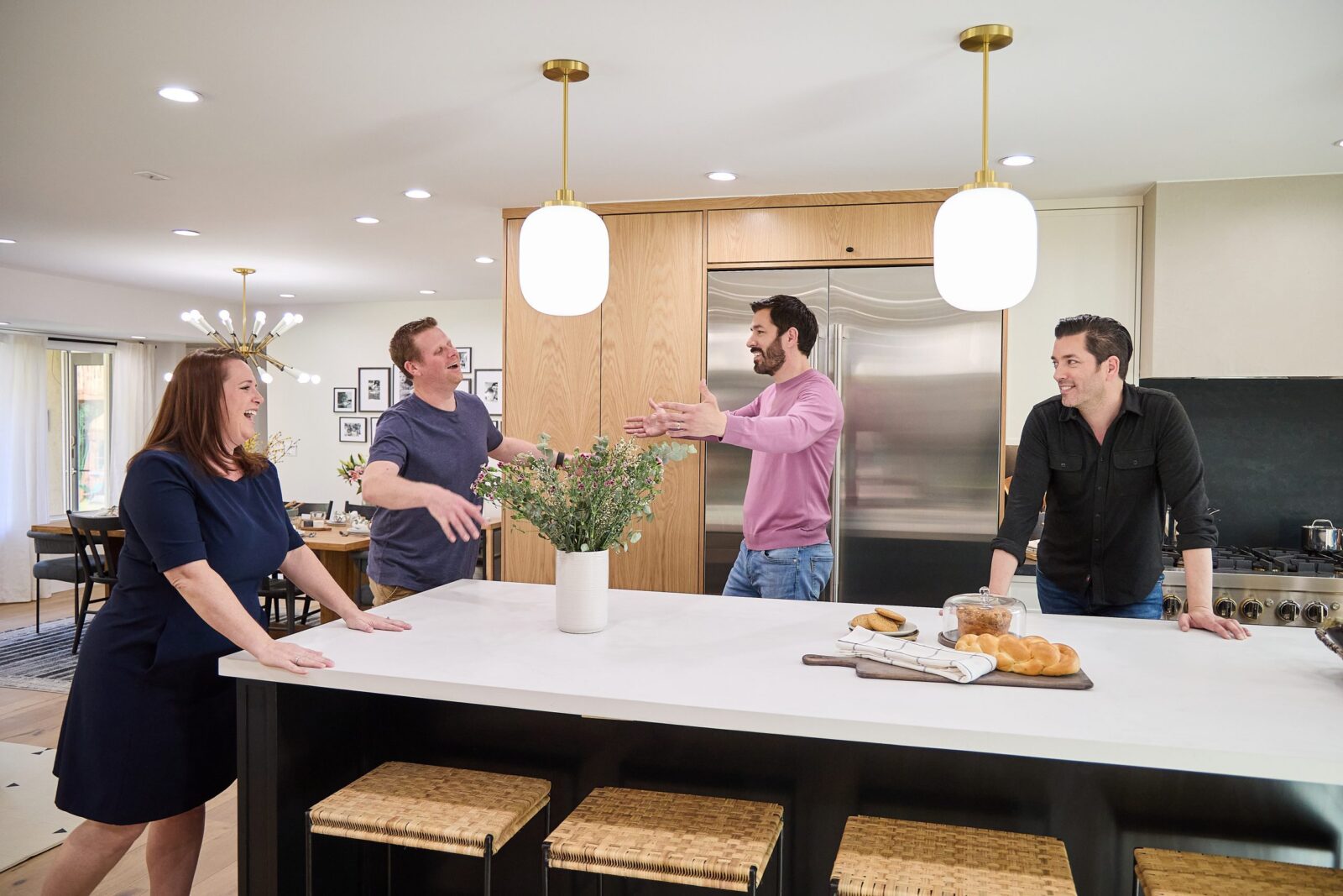 Group of people chatting in a modern kitchen with pendant lights, wood cabinets, and a large island