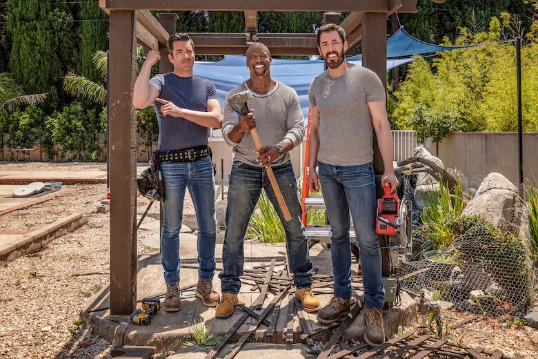 Terry Crews and the Property Brothers standing in a backyard construction area holding tools
