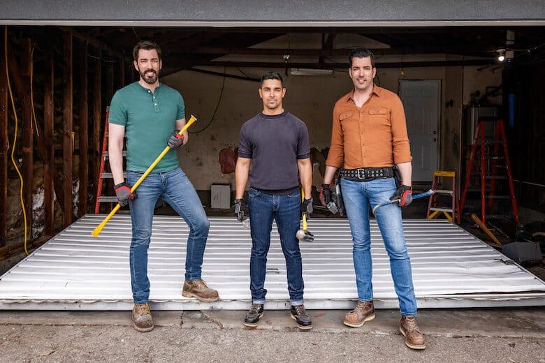 Drew and Jonathan Scott with a man in a garage holding tools, ready for renovation