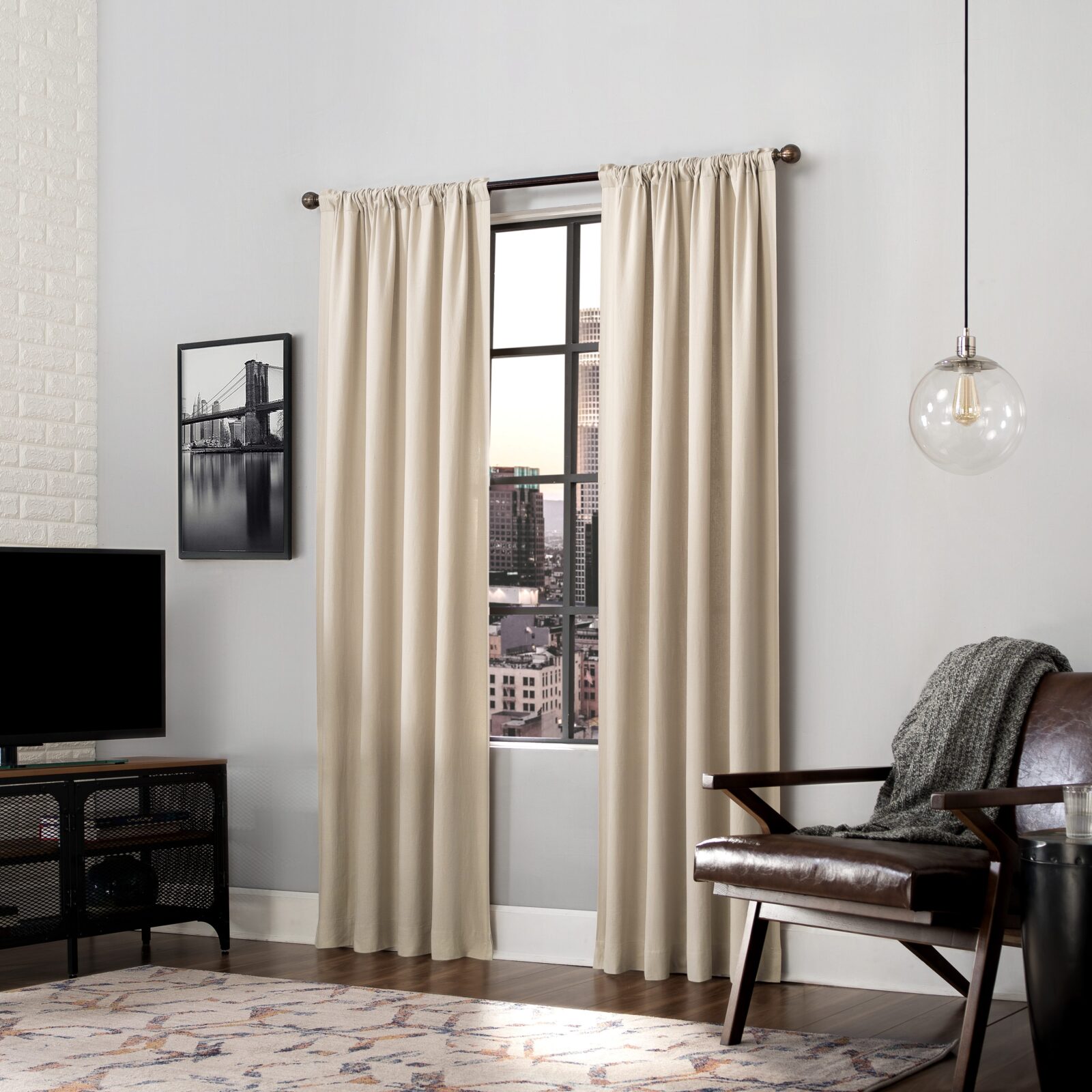 Modern living room with cream curtains, city view window, leather chair, and hanging globe light