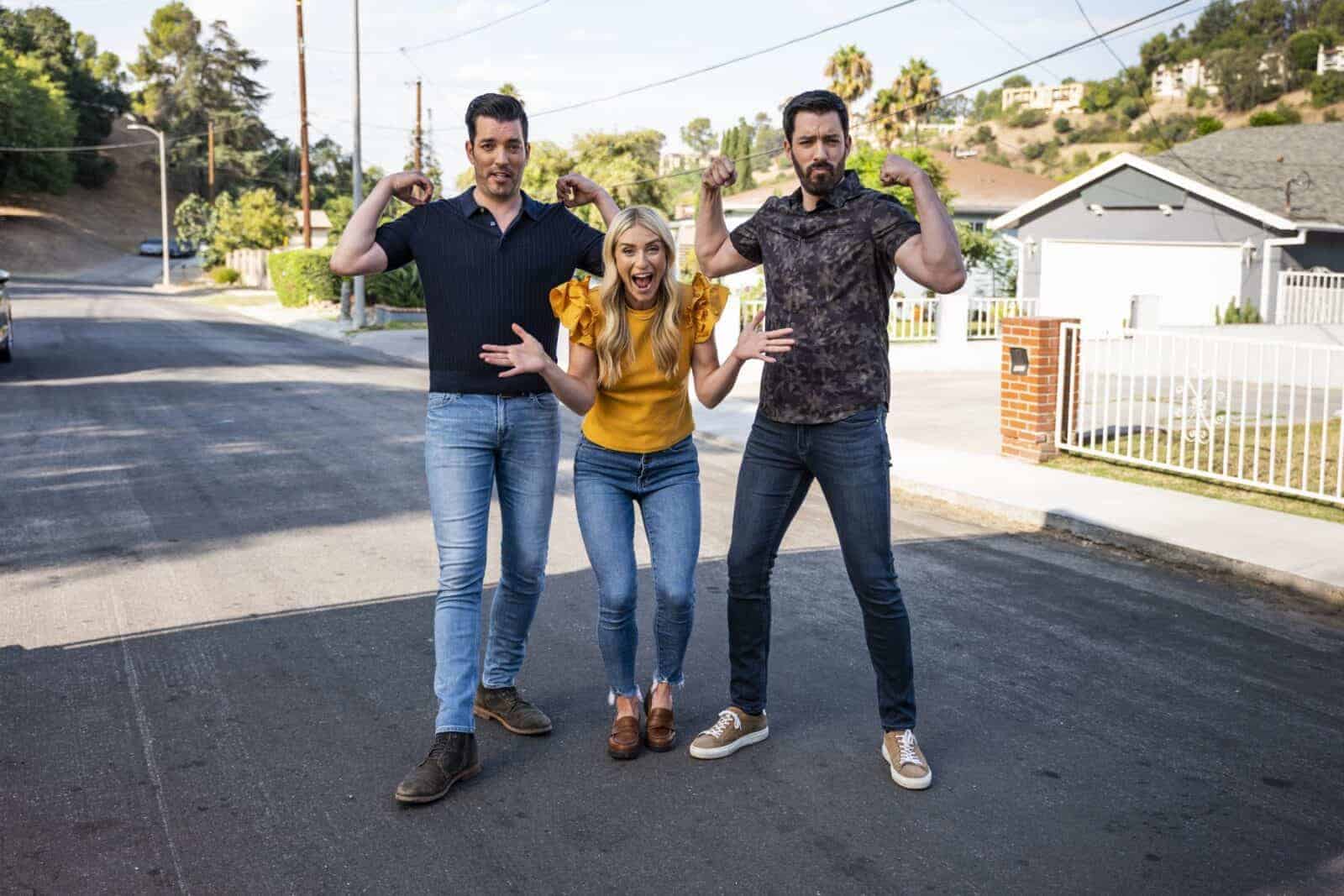 Drew and Jonathan Scott posing playfully with a woman on a suburban street