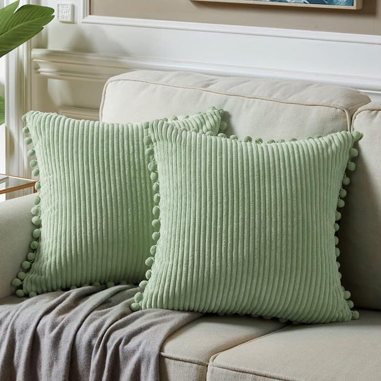 Two green ribbed throw pillows with pom-pom trim on a beige sofa