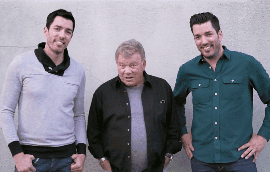 Drew and Jonathan Scott standing with an older man in front of a light gray wall
