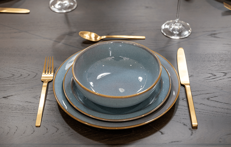 Elegant place setting with blue ceramic dishes and gold flatware on dark wood table