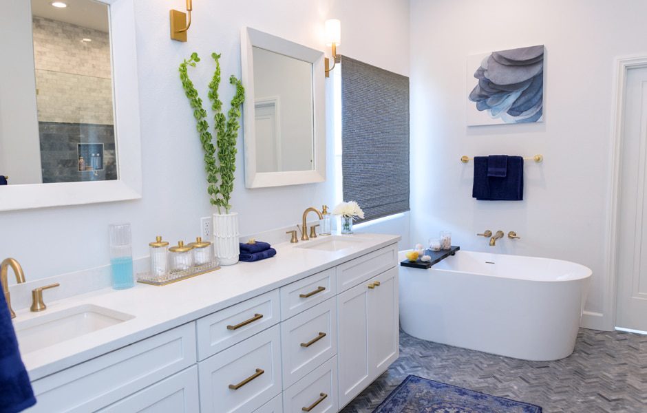 Modern bathroom with white double vanity, freestanding tub, gold fixtures, and blue accents