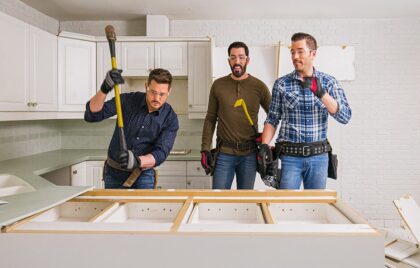 Drew and Jonathan Scott begin kitchen demolition with a third man, removing old cabinetry in a white-tiled space