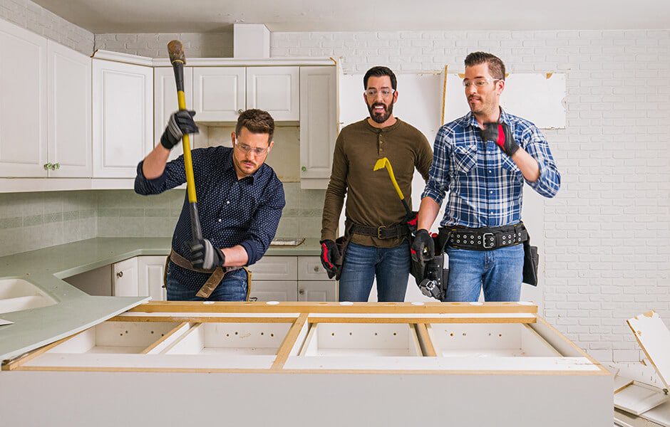 Drew and Jonathan Scott begin kitchen demolition with a third man, removing old cabinetry in a white-tiled space