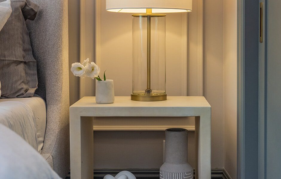 Nightstand with glass lamp, white flowers in a vase, and decorative vase below