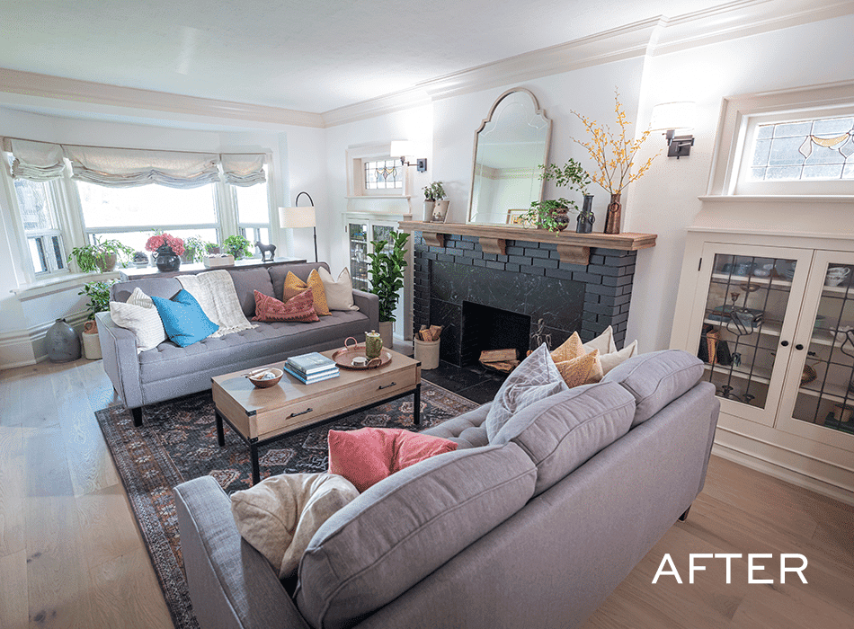 Bright living room with gray sofas, colorful pillows, a black fireplace, and a wooden coffee table
