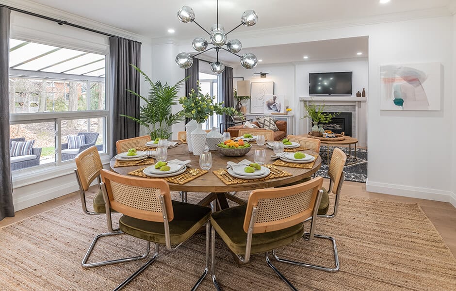 Bright dining room with a round wooden table, modern chandelier, and view into a cozy living room