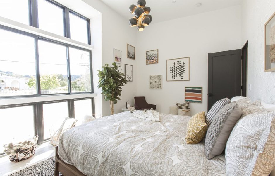 Bright bedroom with large black-framed windows, patterned bedding, wall art, and modern decor