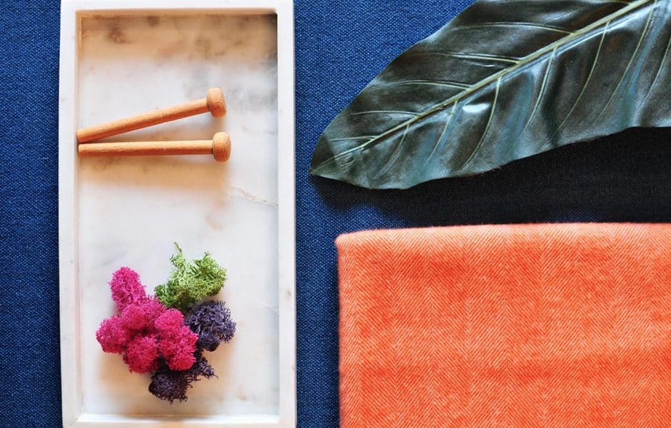 Marble tray with wooden pegs and moss beside a leaf and orange fabric on blue background