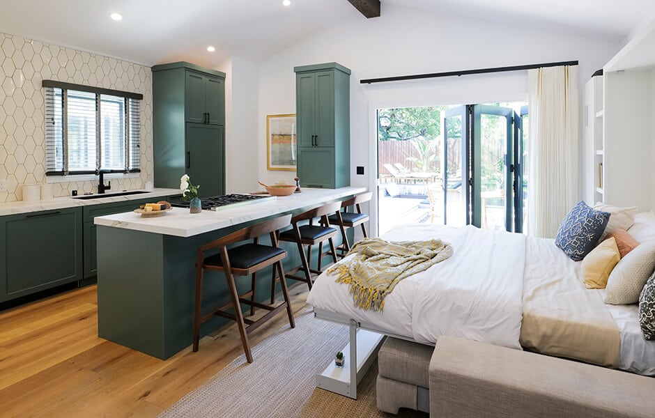 Studio with green kitchen cabinets, island, bed, and sliding glass doors