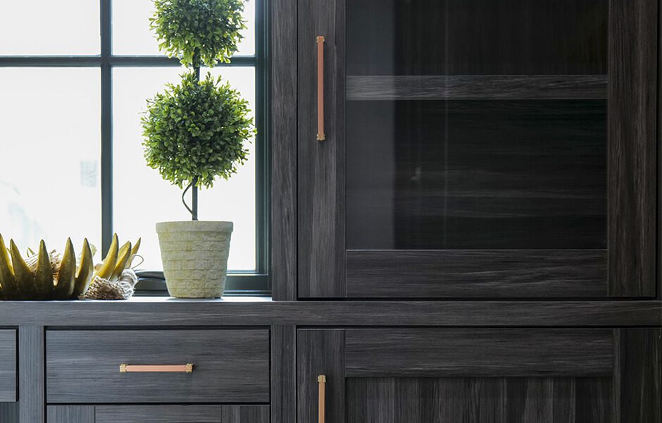 Dark wood cabinet with glass doors, gold handles, and a potted topiary by a window