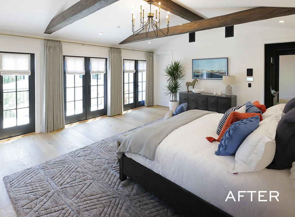 Spacious bedroom with beamed ceiling, large windows with curtains, and a bed with colorful pillows