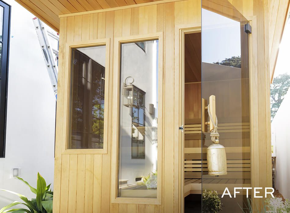 Modern wooden sauna with glass door and windows, featuring a hanging bucket inside