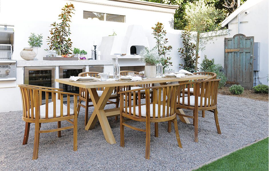 Outdoor dining area with wooden table and chairs, built-in grill, and white pizza oven