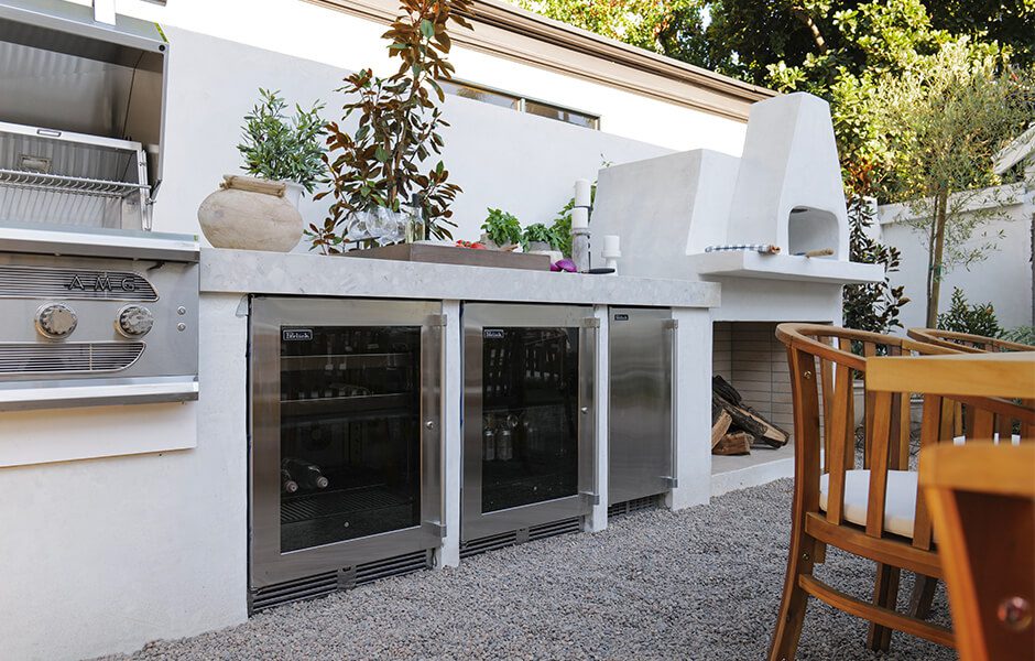 Outdoor kitchen with stainless steel grill, under-counter refrigerators, and a white pizza oven