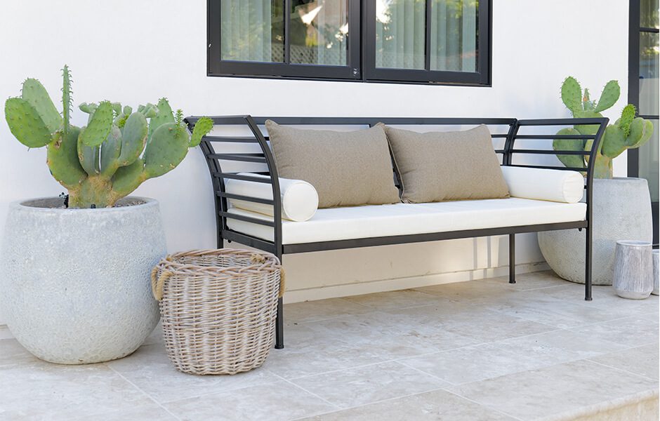 Outdoor bench with beige cushions, flanked by large potted cacti and a wicker basket