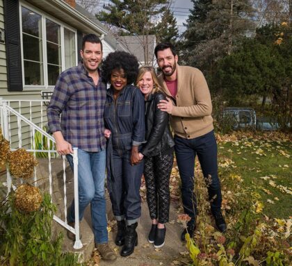 Four people standing together outside a house, smiling and posing for a photo