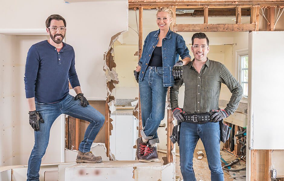 Three people in work clothes and gloves standing in a partially demolished room during renovation
