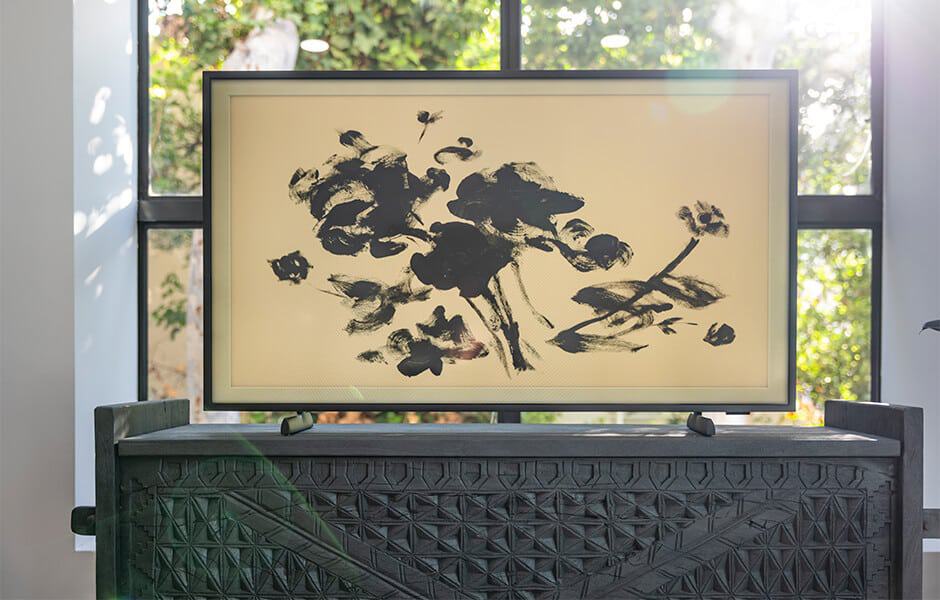 Television displaying black floral artwork on a beige background, set on a carved wooden console