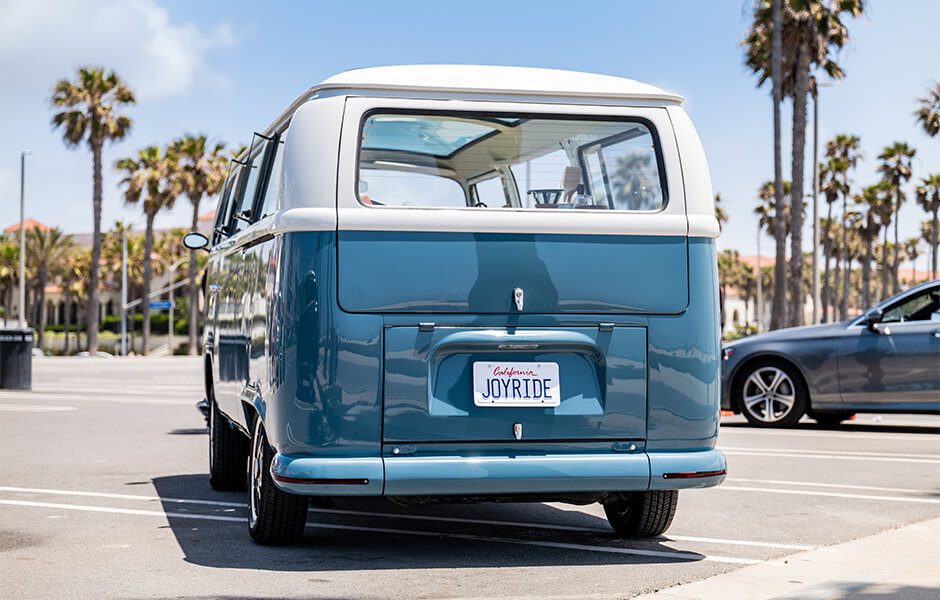 Rear view of a blue and white vintage Volkswagen van with a California license plate reading “JOYRIDE."