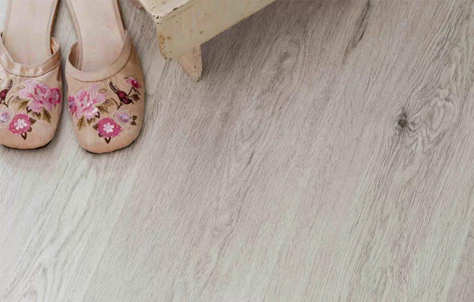 Light wood grain flooring with beige embroidered floral slippers beside a piece of furniture