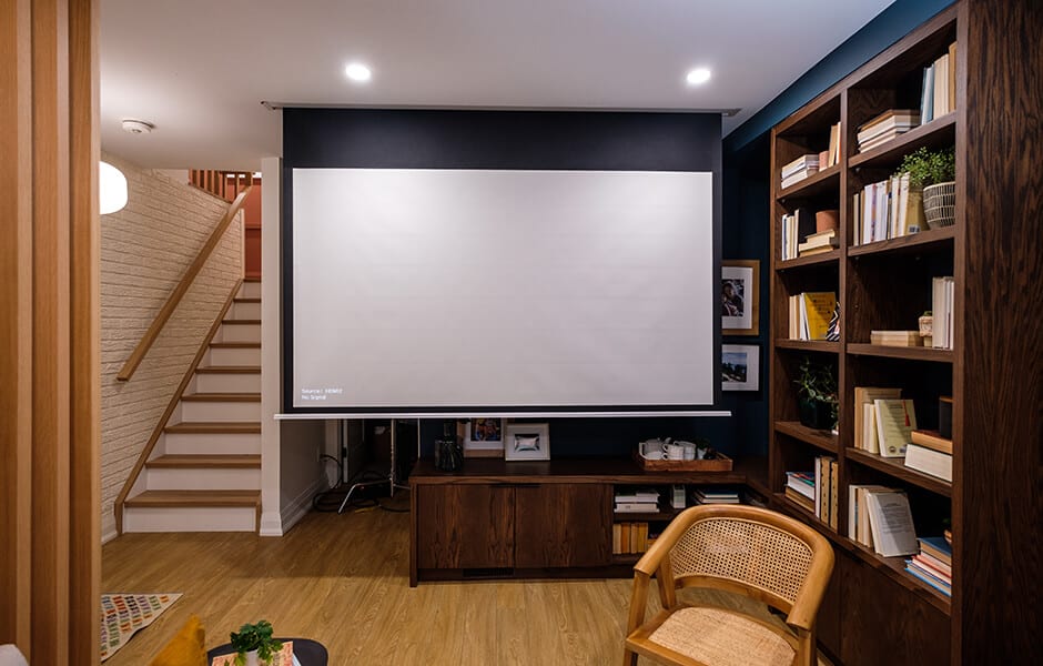 Cozy home theater room with a pull-down projector screen, wooden bookshelves, and staircase nearby