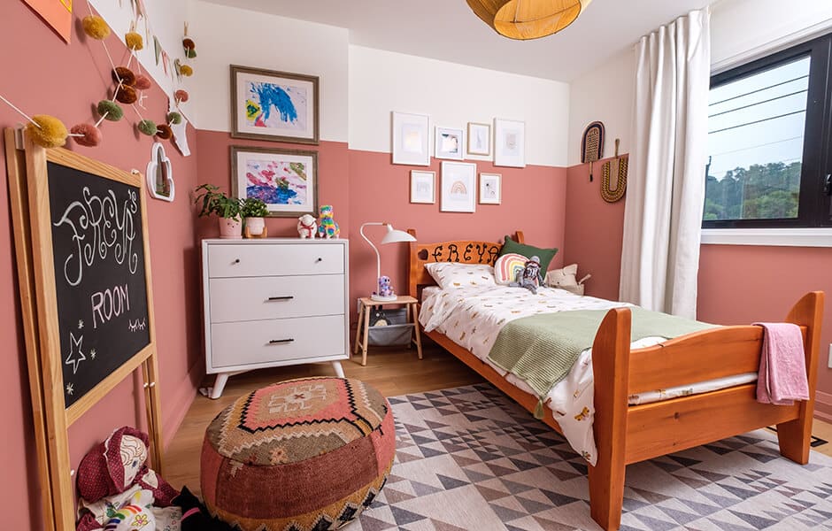 Cozy kids' bedroom with a wooden bed, pink walls, white dresser, chalkboard, and colorful wall art