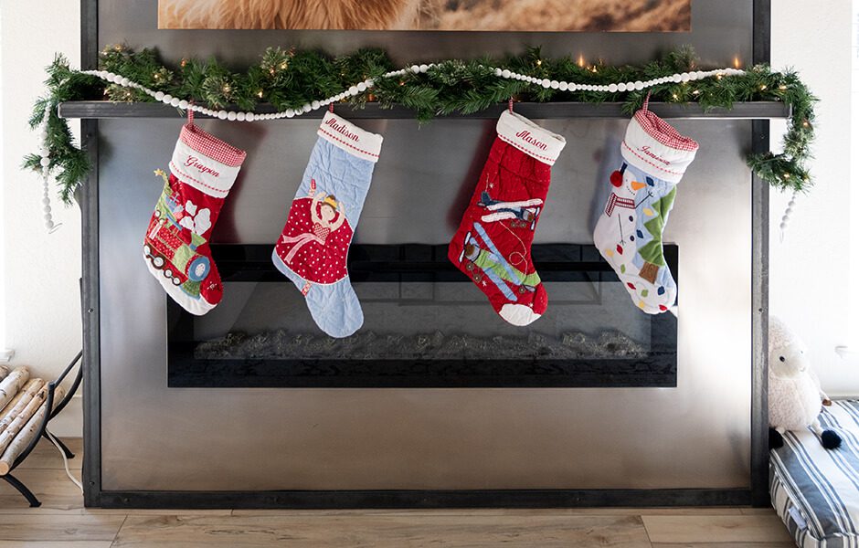 Fireplace decorated with garland and four Christmas stockings hanging from the mantel