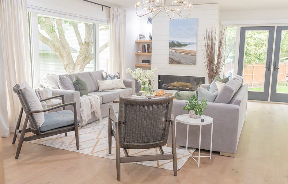 Bright living room with gray sofas, modern chairs, a fireplace, and large windows bringing in natural light
