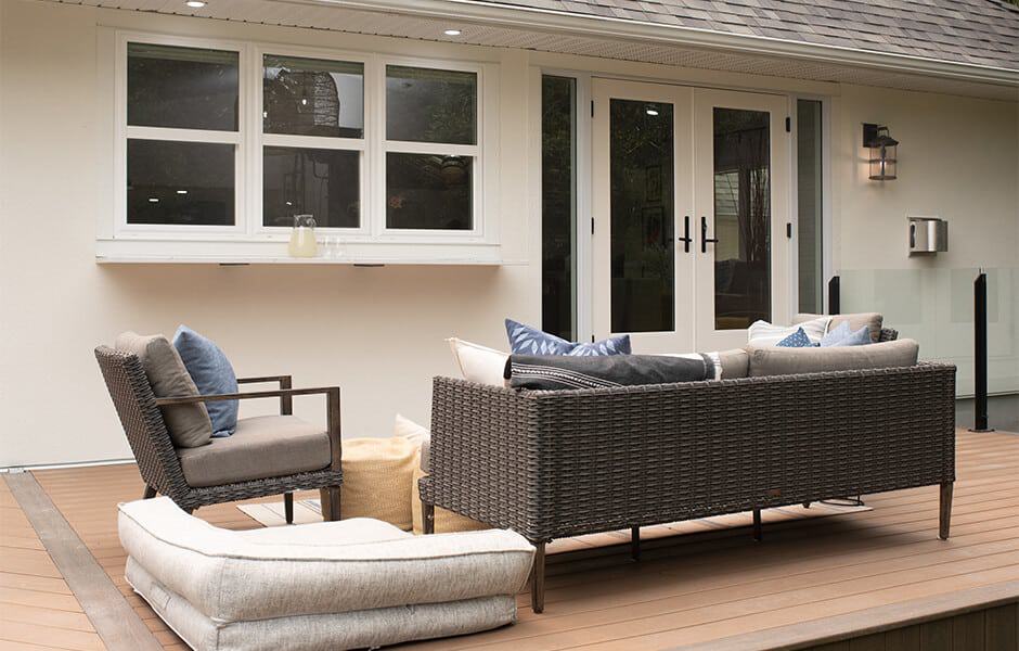 Outdoor patio with wicker furniture, cushioned seating, and neutral decor against a white house exterior