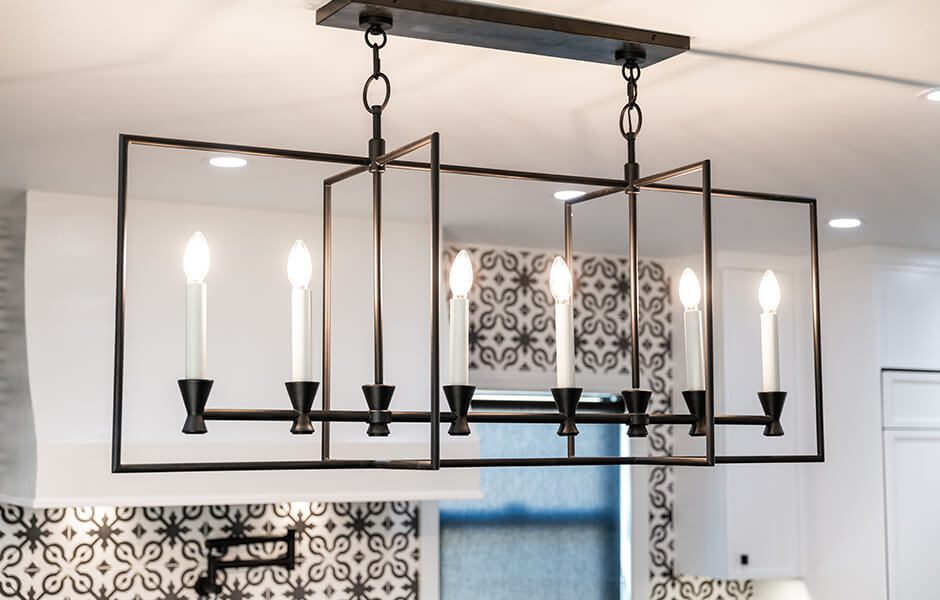Rectangular black metal chandelier with six candle-style light bulbs hanging in a kitchen