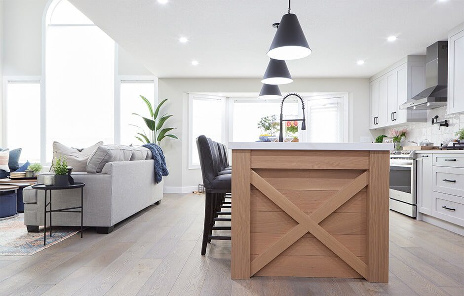 Open-concept kitchen and living area with a wood island, black pendant lights, white cabinets, and a gray sofa