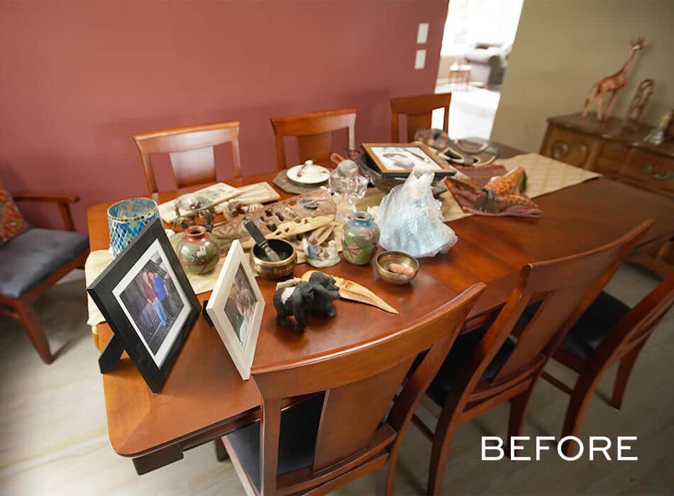 Cluttered dining room with a wooden table covered in framed photos, pottery, and decorative items