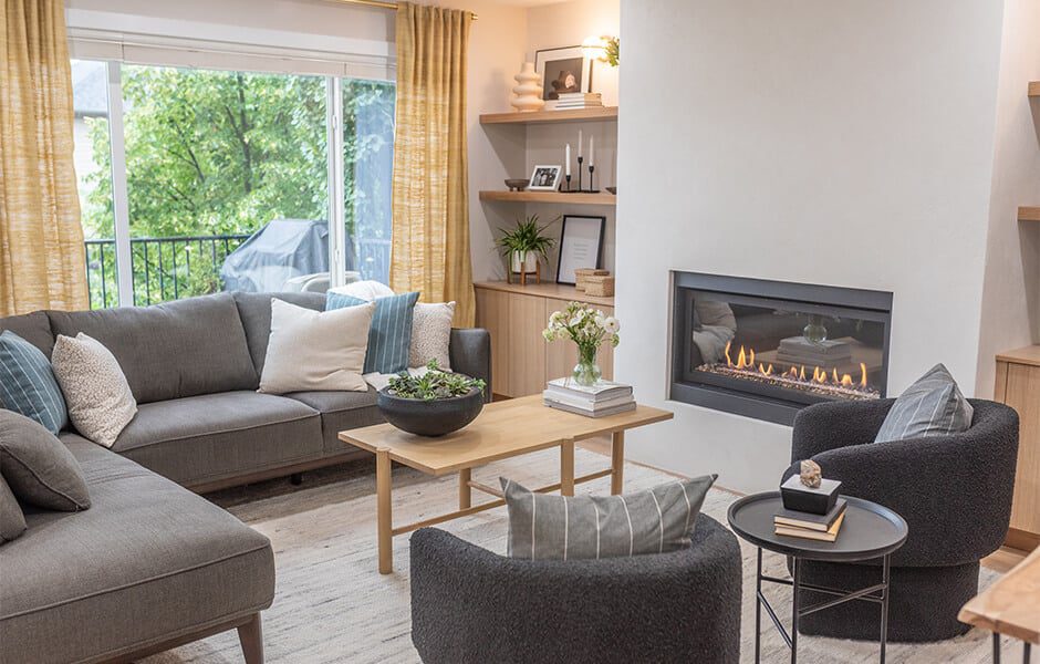 Cozy living room with gray sofas, round chairs, a wooden coffee table, built-in shelves, and a modern fireplace