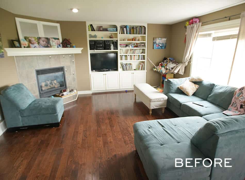 Living room with teal sectional sofa, fireplace, built-in shelves with books and TV, and clutter by the window