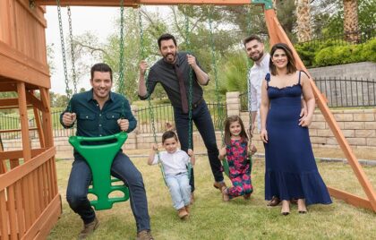 Family with children and two men on swings smiling together in a backyard playset