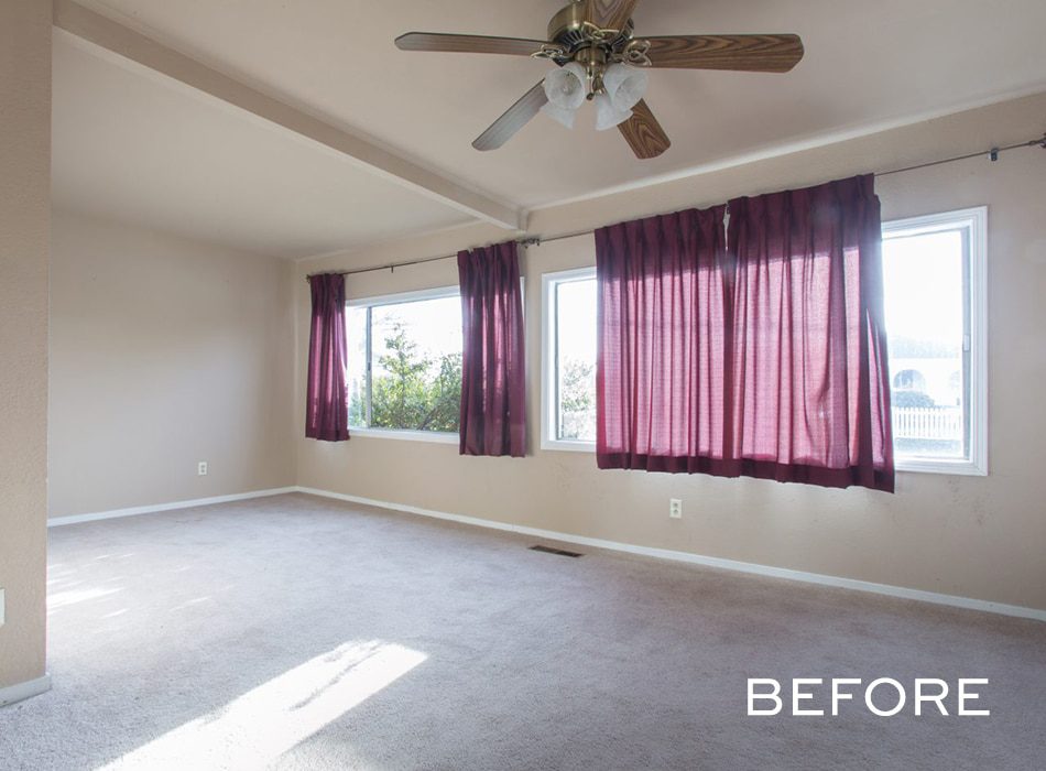 Empty room with beige walls, carpet flooring, maroon curtains, and a ceiling fan