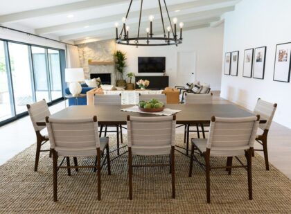 Open-concept dining and living room with large table, white chairs, and modern chandelier