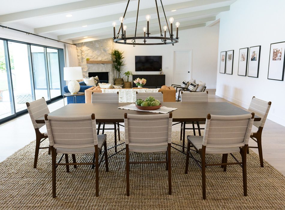 Open-concept dining and living room with large table, white chairs, and modern chandelier