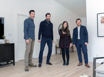 Scott brothers, a man, and a woman standing in a modern living room with light wood floors and white walls