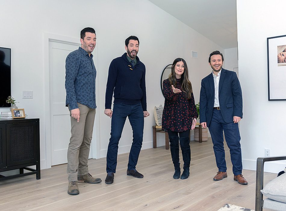 Scott brothers, a man, and a woman standing in a modern living room with light wood floors and white walls